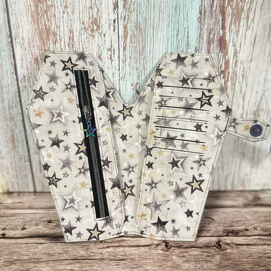 Interior view of a tall, handmade coffin-shaped wallet crafted from black, gold, and white star-print cork fabric. The left panel features a black zipper pocket with a rainbow-finish star-shaped zipper pull. The right panel includes 8 horizontal card slots, with a cash slot hidden behind each side. The coffin-shaped snap tab closure with rainbow snap is visible on the right.
