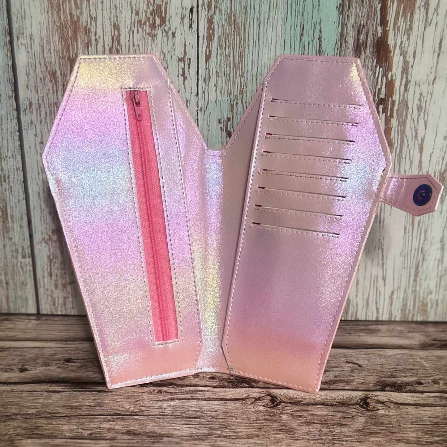 Interior view of a tall handmade coffin-shaped wallet crafted in shimmering iridescent vinyl with soft pink undertones. The right panel features 8 neatly stitched card slots with a full cash pocket behind, while the left panel includes a pink zipper pouch and an additional cash pocket behind it. The snap tab closure with a rainbow snap is visible on the right side.