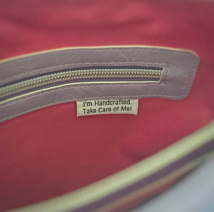 Close-up of the interior zipper pocket on a handmade tote bag. The zipper is trimmed with lavender faux leather and silver hardware. Below the zipper, a fabric tag reads, 'I'm Handcrafted. Take Care of Me!' against a bright pink fabric lining.